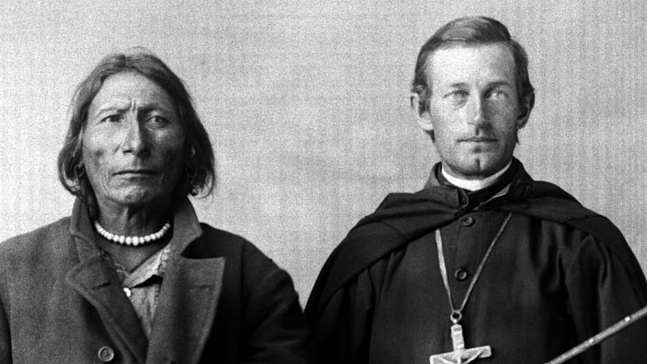 Das Bild zeigt einen Indigenen neben einem christlichen Geistlichen; Zwangskonvertierungen sind Teil von Unterdrückung und Rassismus.